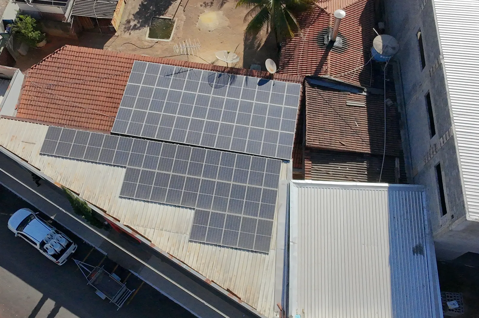 Vista aérea de telhado residencial com dois conjuntos de módulos fotovoltaicos instalados sobre telha cerâmica e fibrocimento